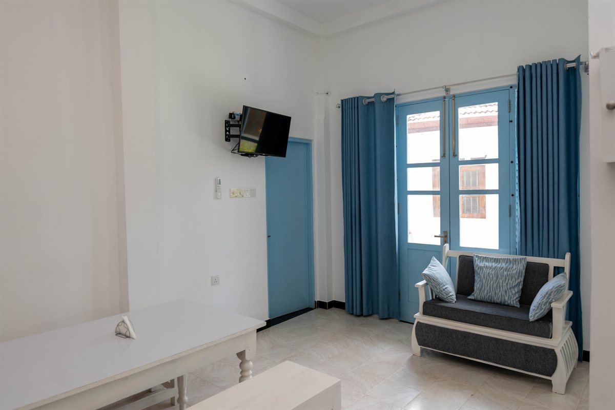 Living and dining corner with a sofa, television and white table at Tropical Garden Retreat