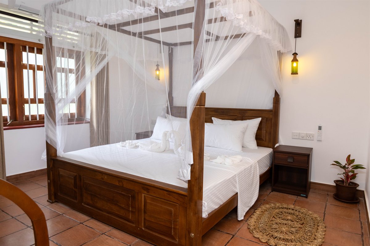 Wooden four-poster bed with white linens and a mosquito net at Heritage House Retreat